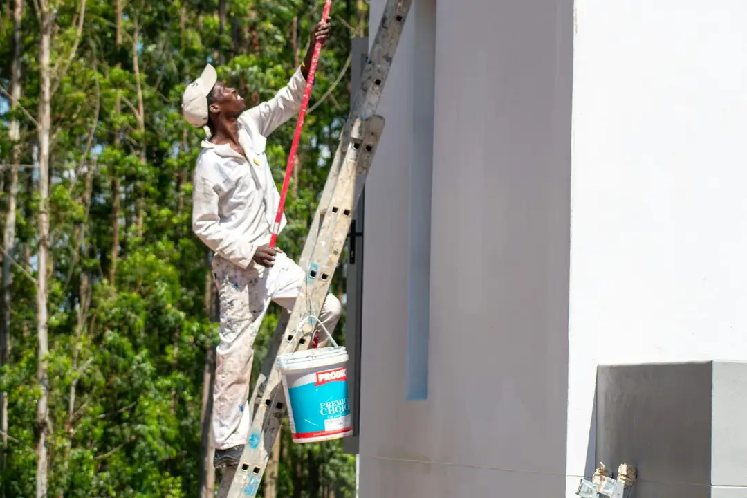 Painter on a ladder painting the exterior wall of a house among gum trees