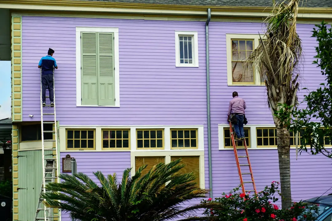 Two painters on ladders repainting a weatherboard house