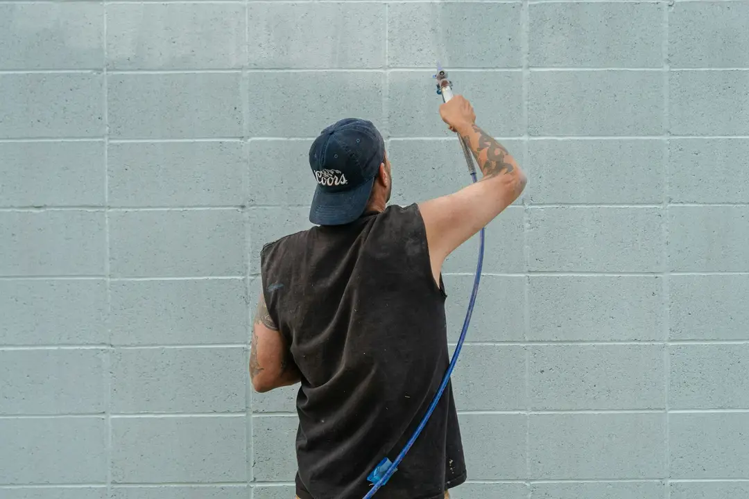 Painter using an airless sprayer on a block wall